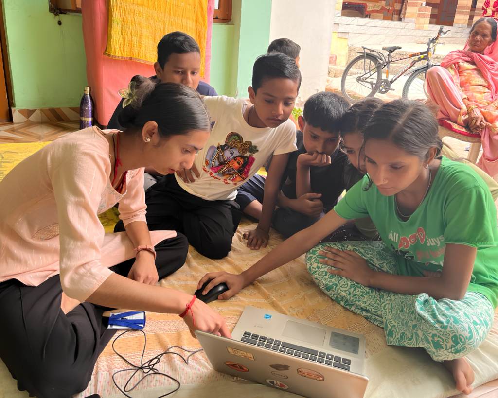Children in Sukkar village gather at an EIF Learning Hub as a young girl receives practical digital skills training on a laptop in Dharamshala.