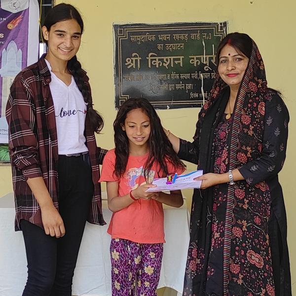 Mrs. Indu Sharma, Sarpanch of Rakkar village, distributing an activity certificate to a young rural girl alongside an EIF local women community leader.